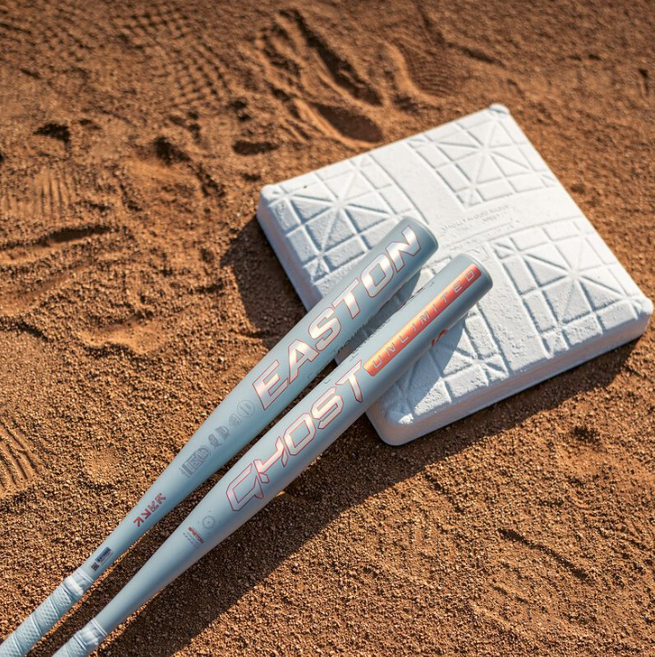 A photo of the 2025 Easton Ghost Unlimited -10 Fastpitch Softball Bat in colour white and orange. Outside view near baseball plate.