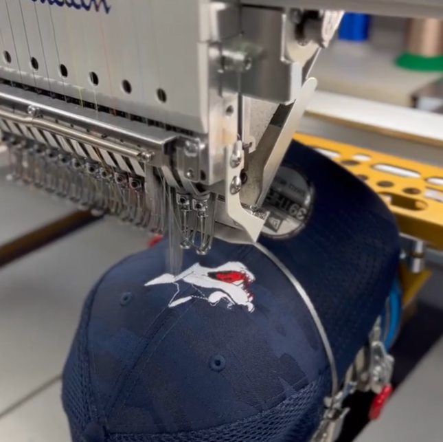 A photo of a custom navy blue Sudbury Wolves hat being sewn together with our embroider machine.