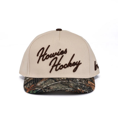 A photo of the Howies The Sharpshooter Lid in colour cream with a brown logo and a camo brim.