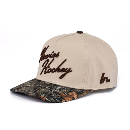 A photo of the Howies The Sharpshooter Lid in colour cream with a brown logo and a camo brim.