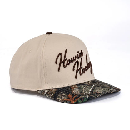 A photo of the Howies The Sharpshooter Lid in colour cream with a brown logo and a camo brim.