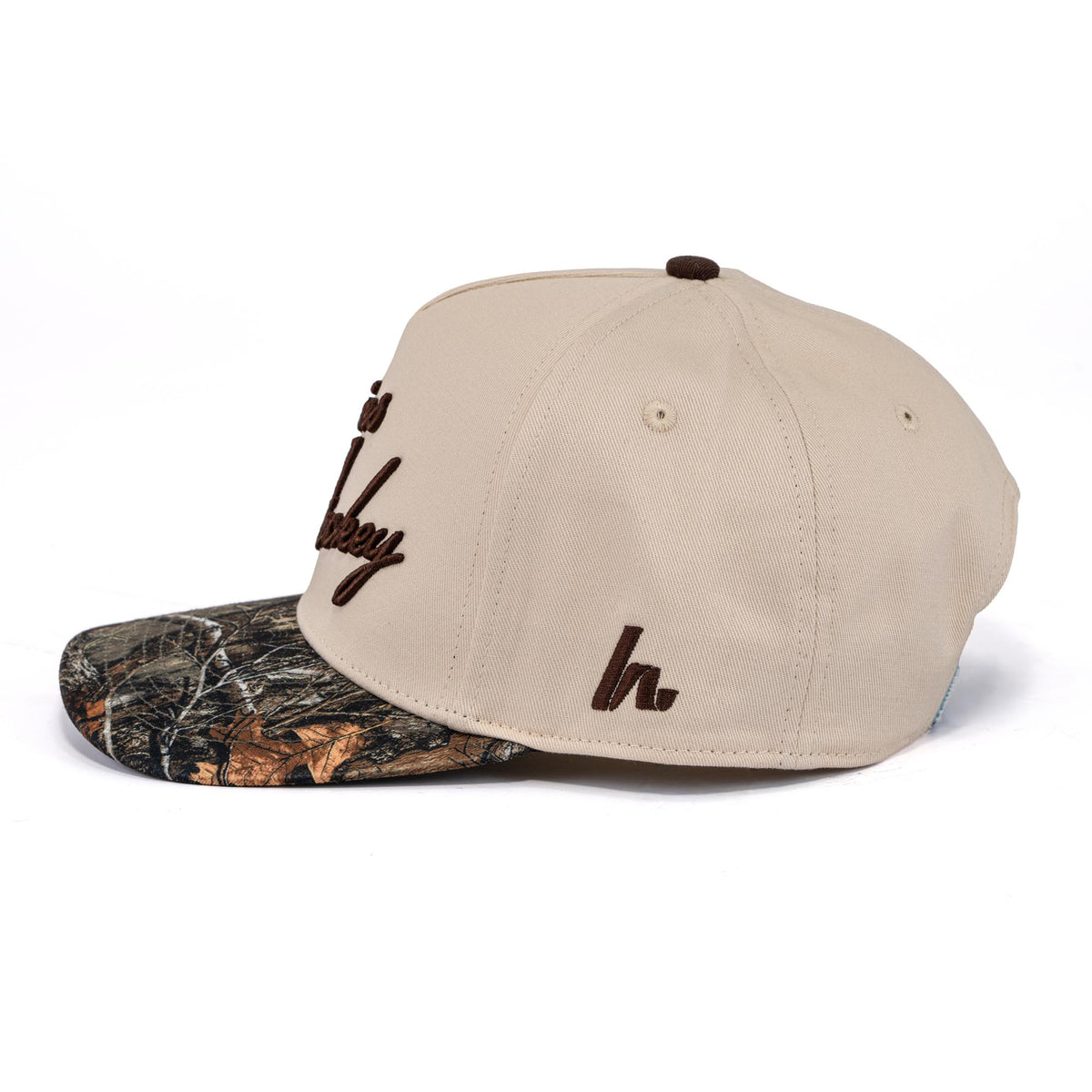 A photo of the Howies The Sharpshooter Lid in colour cream with a brown logo and a camo brim.