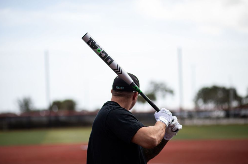 A photo of the 2024 Miken DC-41 SUPERMAX USSSA Slo-Pitch Bat - Source Exclusive in silver colour with dark green text with batter preparing to swing on the diamond. 