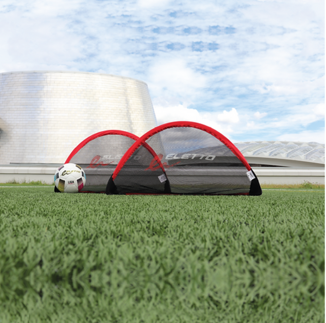 A photo of the Eletto Pop-Up Goal Set - Small in colour red and black. Positioned in a field. 