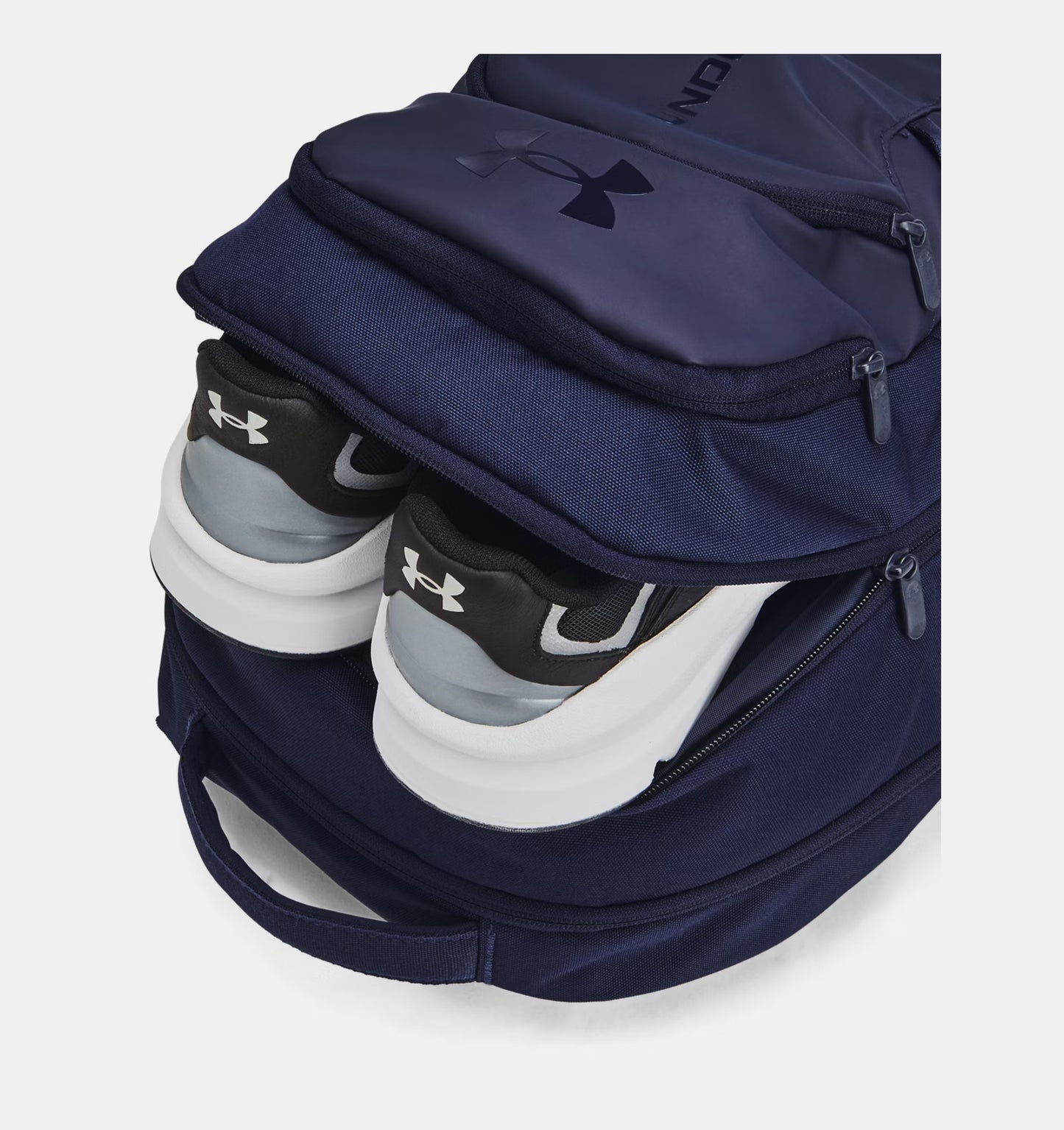Navy Under Armour backpack shown with running shoes in second compartment.